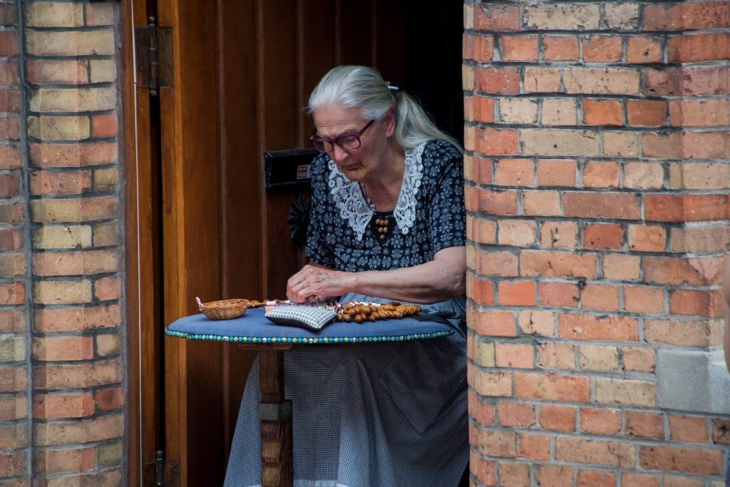 Lace maker seated in a doorway working with bobbins