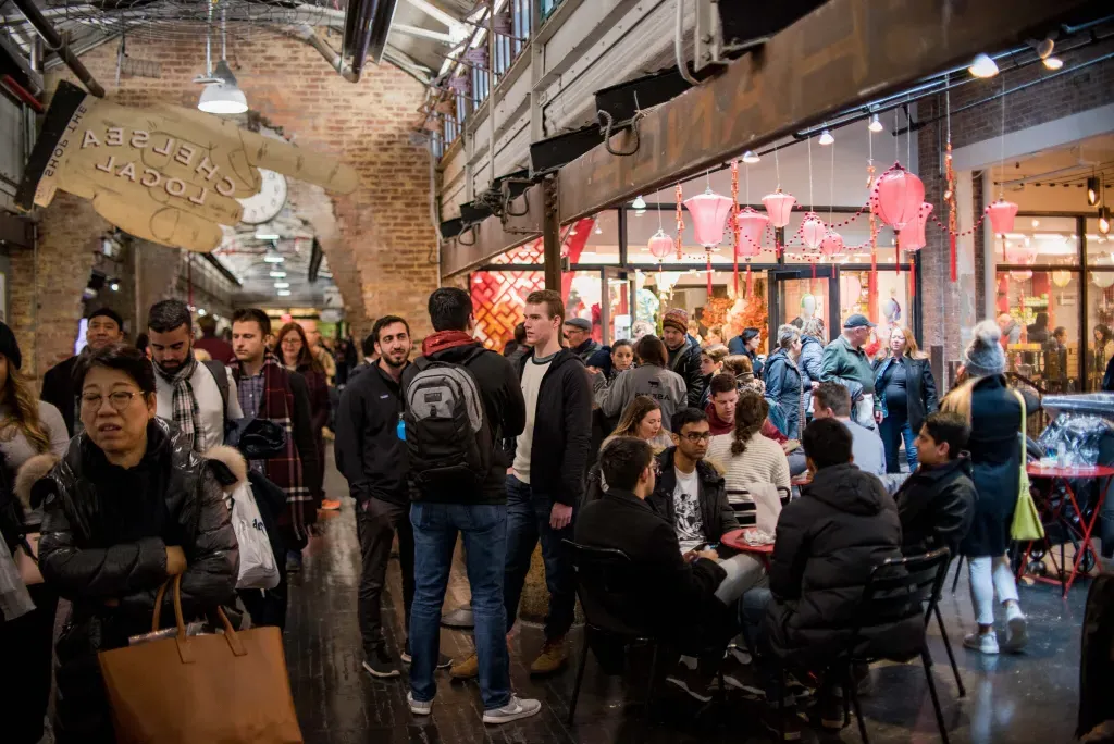 Busy scene inside Chelsea Market with shoppers, diners, and brick archways.