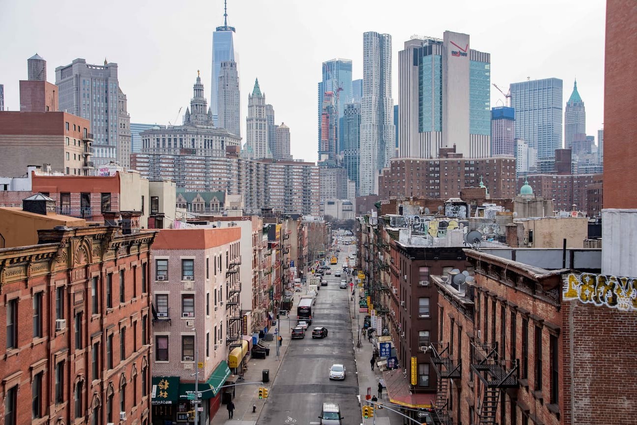 Street view in Chinatown with red-brick buildings and One World Trade Center in the background.