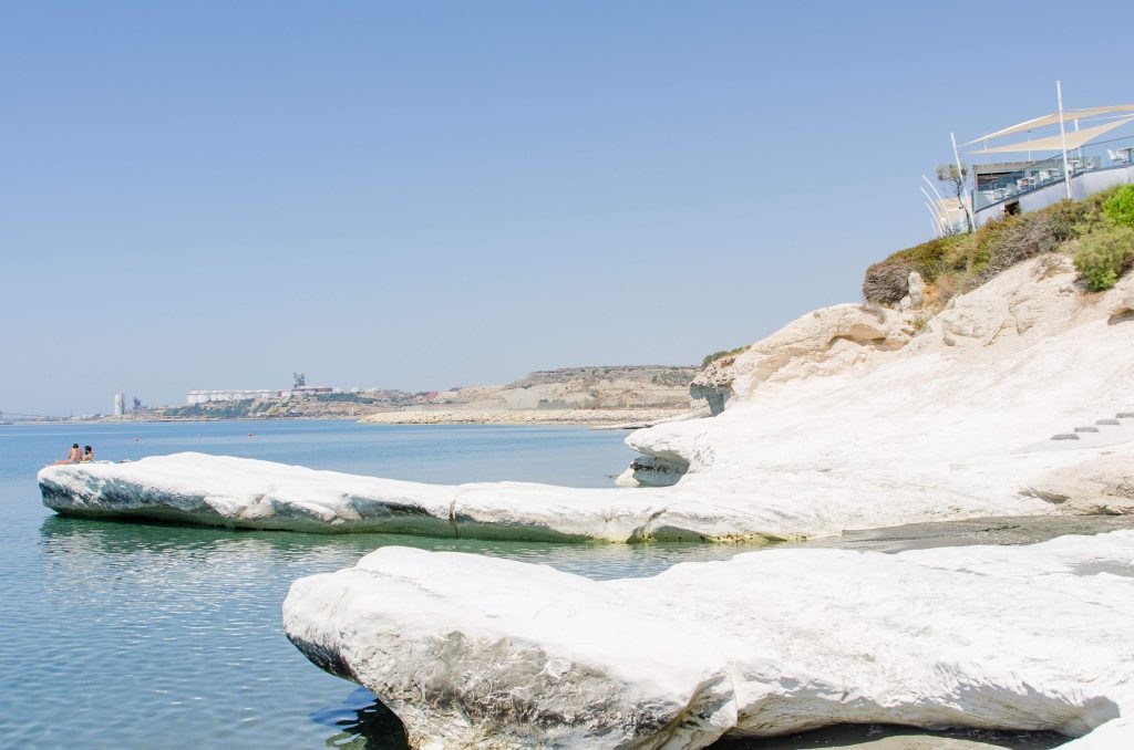 Visitors perched on white coastal cliffs in Cyprus under a cloudless sky.